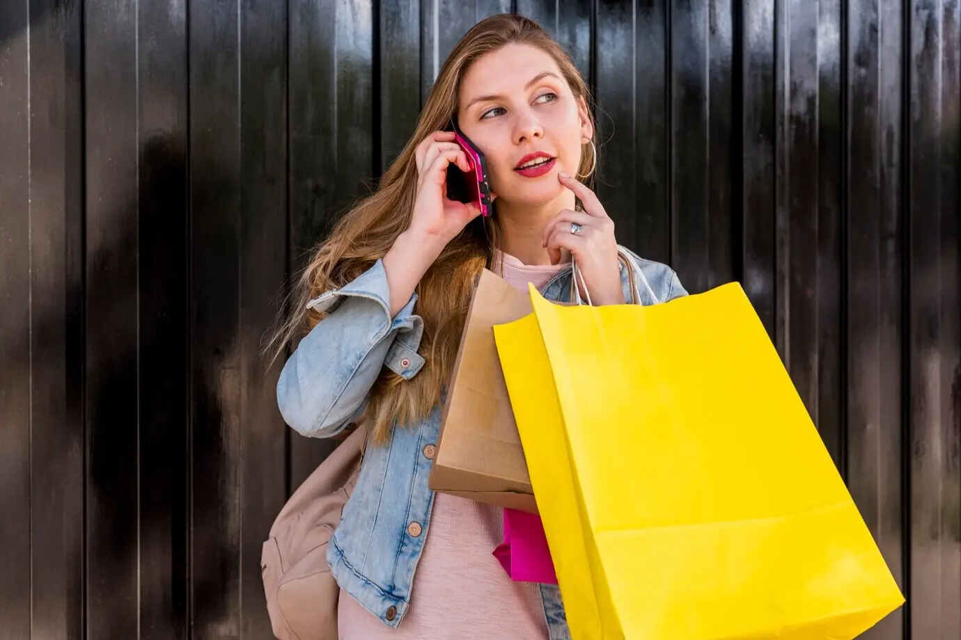 Задумчивая женщина с пакетами с покупками разговаривает по телефону.